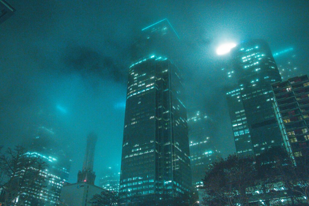 A dramatic cityscape view of skyscrapers shrouded in fog with glowing city lights at night.
