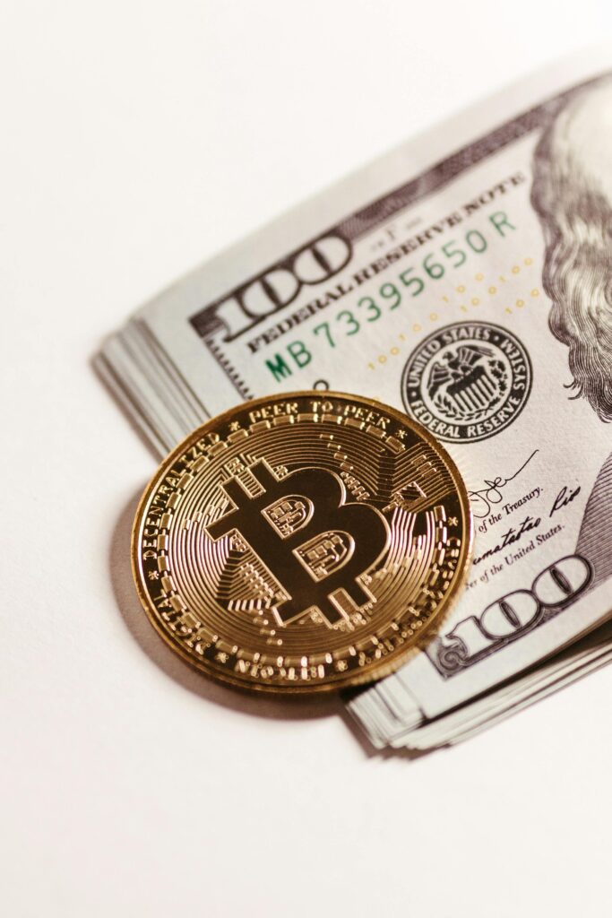 Close-up of a Bitcoin coin on top of hundred dollar bills representing digital and paper currency.