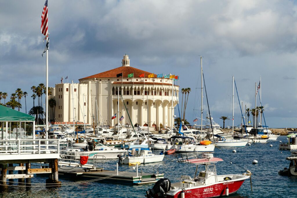 Scenic view of Avalon Harbor featuring the iconic Catalina Casino with boats docked and the American flag waving.