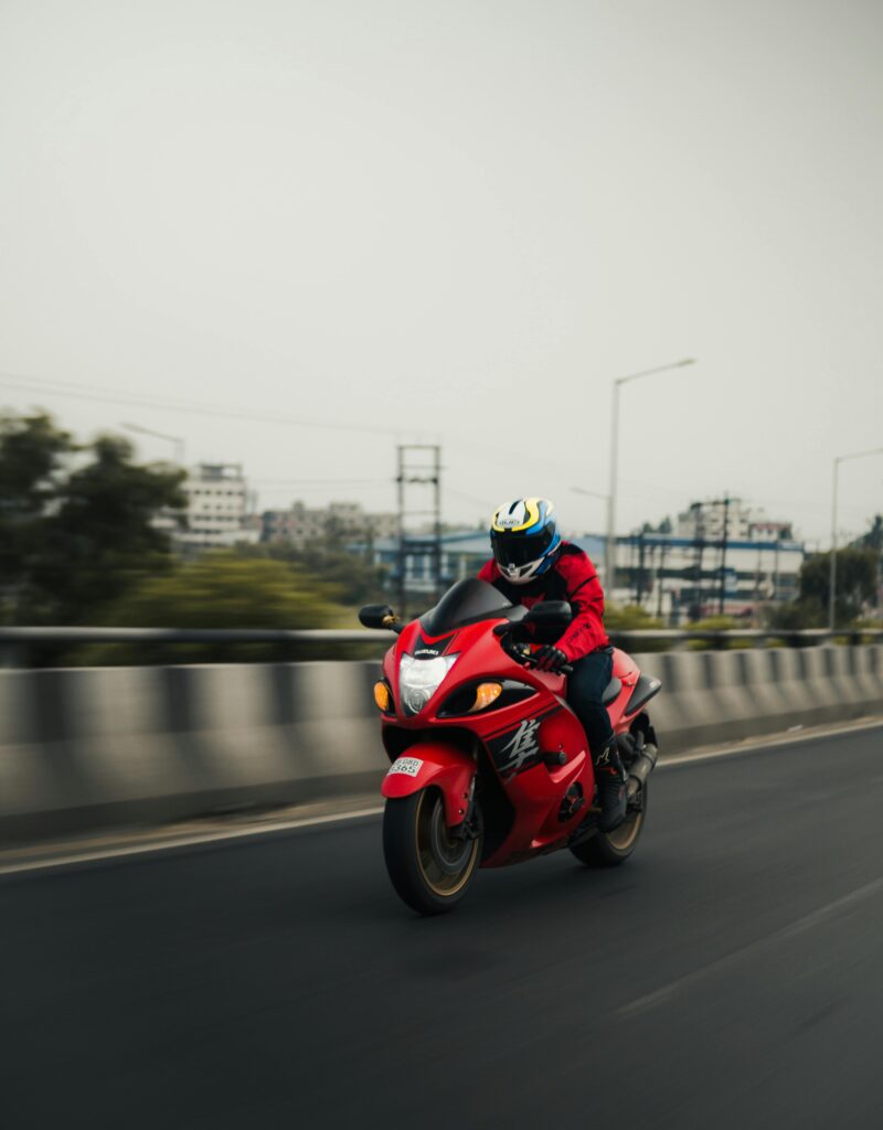 A motorcyclist in a helmet rides a red motorcycle on a city street in Kolkata, displaying urban speed and style.