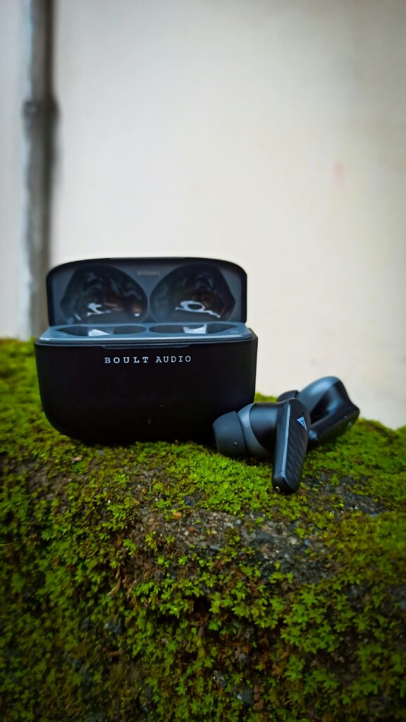 Wireless earbuds case with open lid on a green mossy surface, showing sleek design and texture contrast.