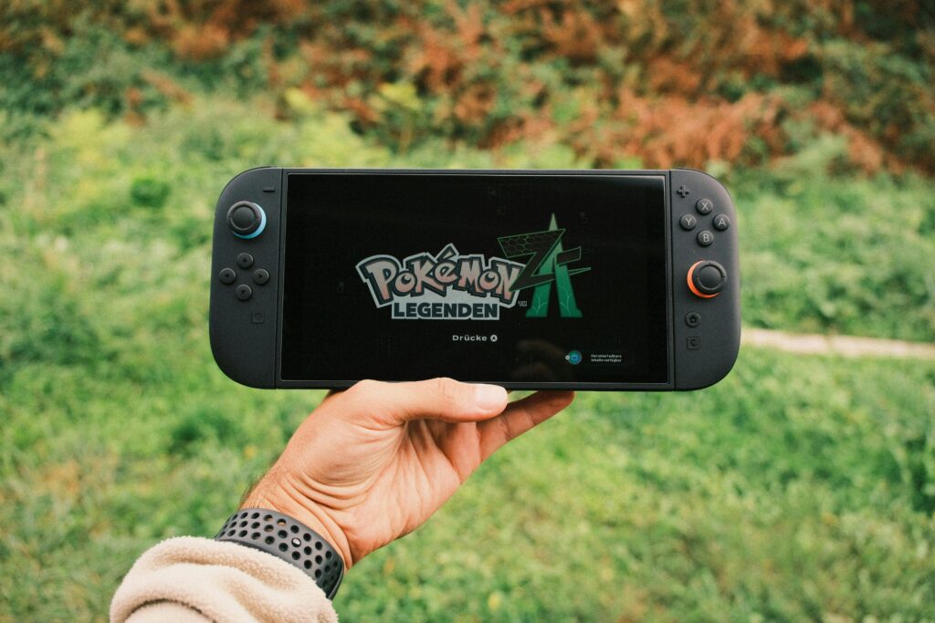 pokemon xd technology in usa A hand holding a handheld gaming console displaying the Pokémon Legends game screen outdoors.