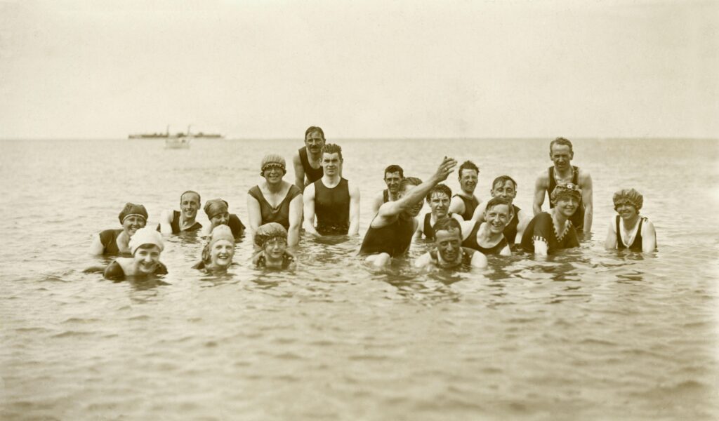 A vintage photo of a joyful group of adults swimming together in the ocean.