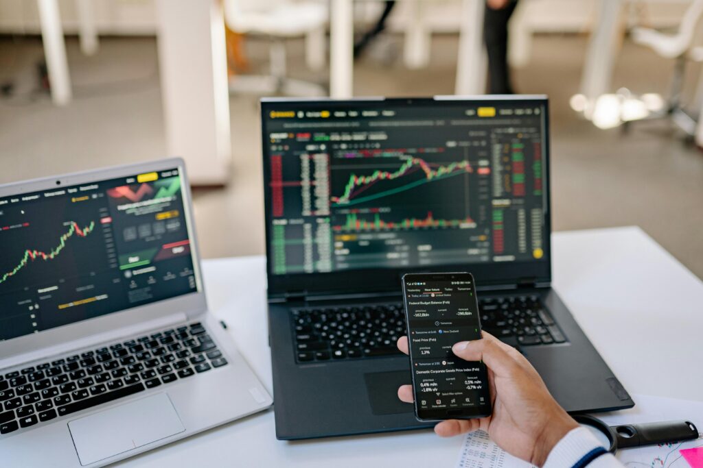 A professional tracks stock market trends using two laptops and a smartphone, showcasing digital finance tools.