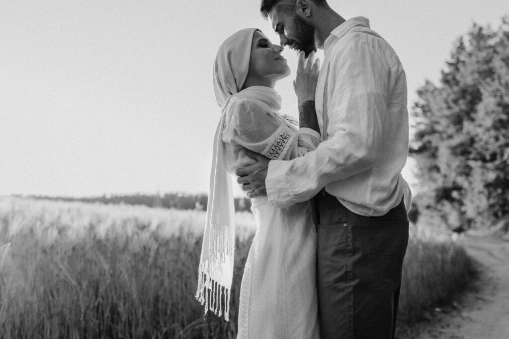 A romantic black and white photo of a couple embracing in a countryside field.