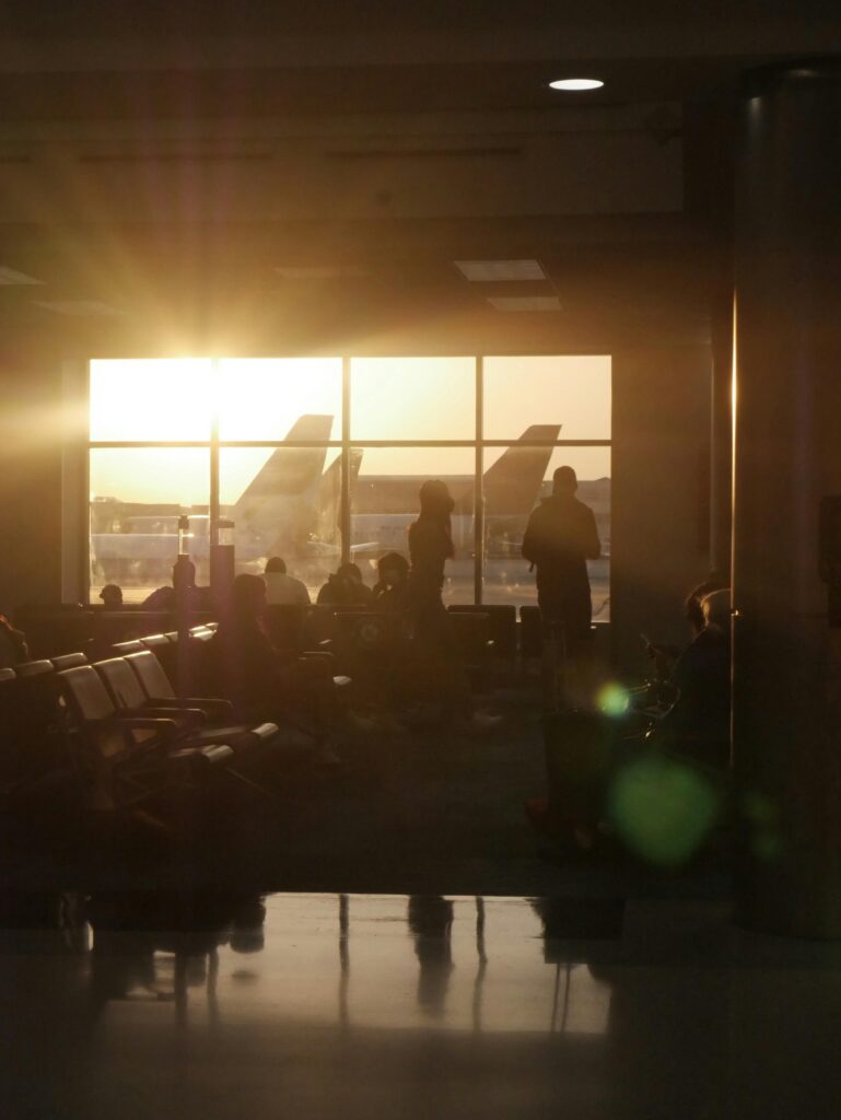 Passengers await flights at Orlando Airport with sunset in the background, creating silhouettes.