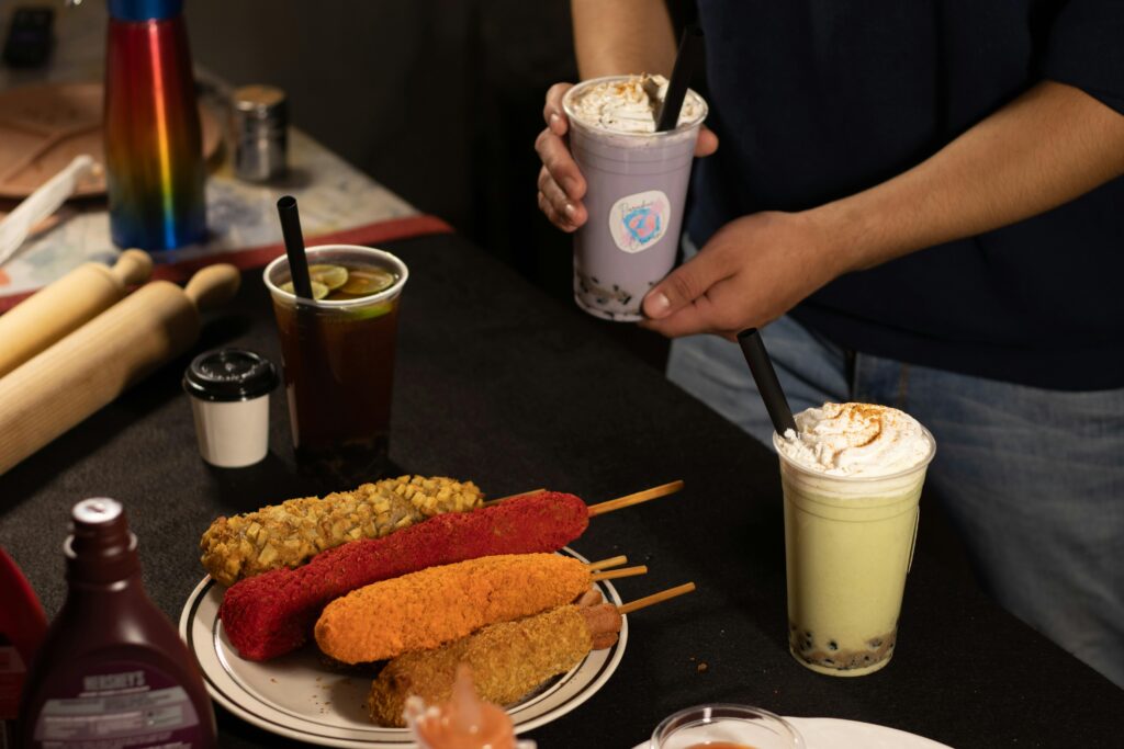 Vibrant boba drinks and assorted corn dogs on a table setup for a casual meal.