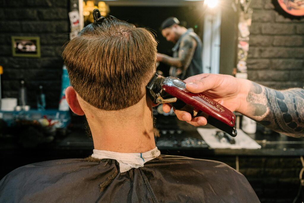 Back view of a man receiving a haircut with clipper in a barber shop.