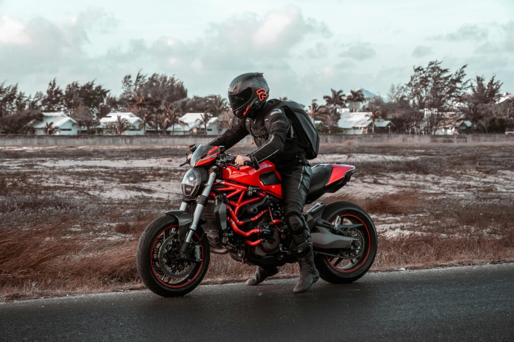 A motorcyclist riding a red Ducati on a rural road with safety gear. Outdoors scene with clear skies.