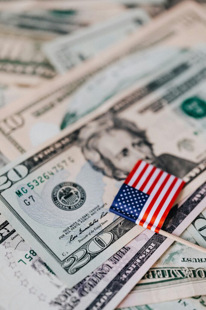 From above composition of tiny American flag placed on pile of United States dollar bills as national currency for business and personal financial operations