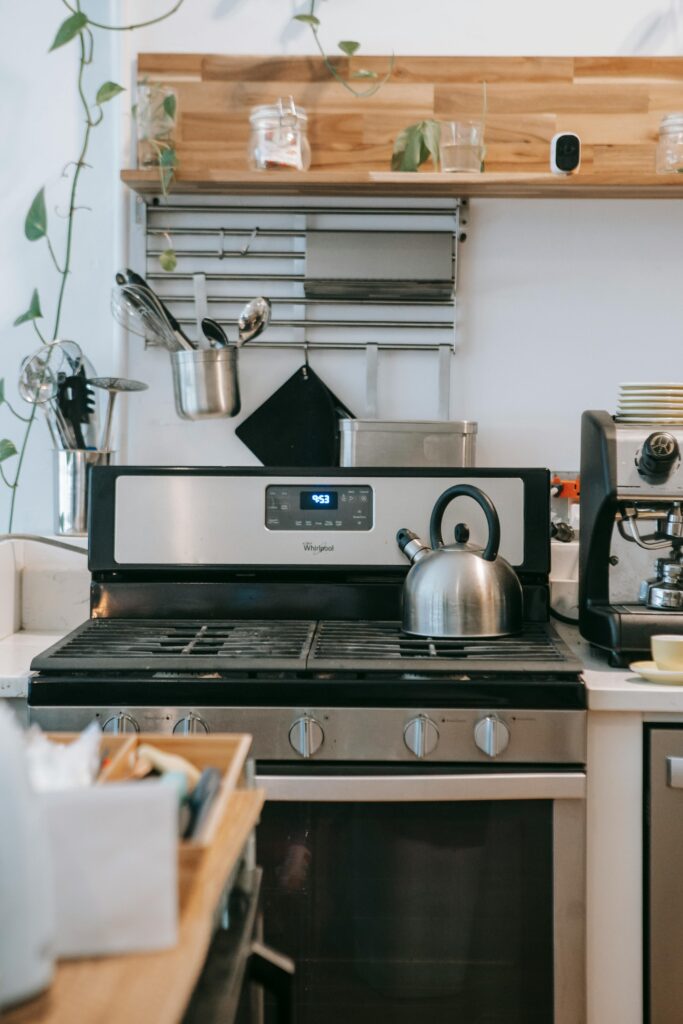 Interior of contemporary light kitchen with gas stove with kettle surrounded with various kitchenware